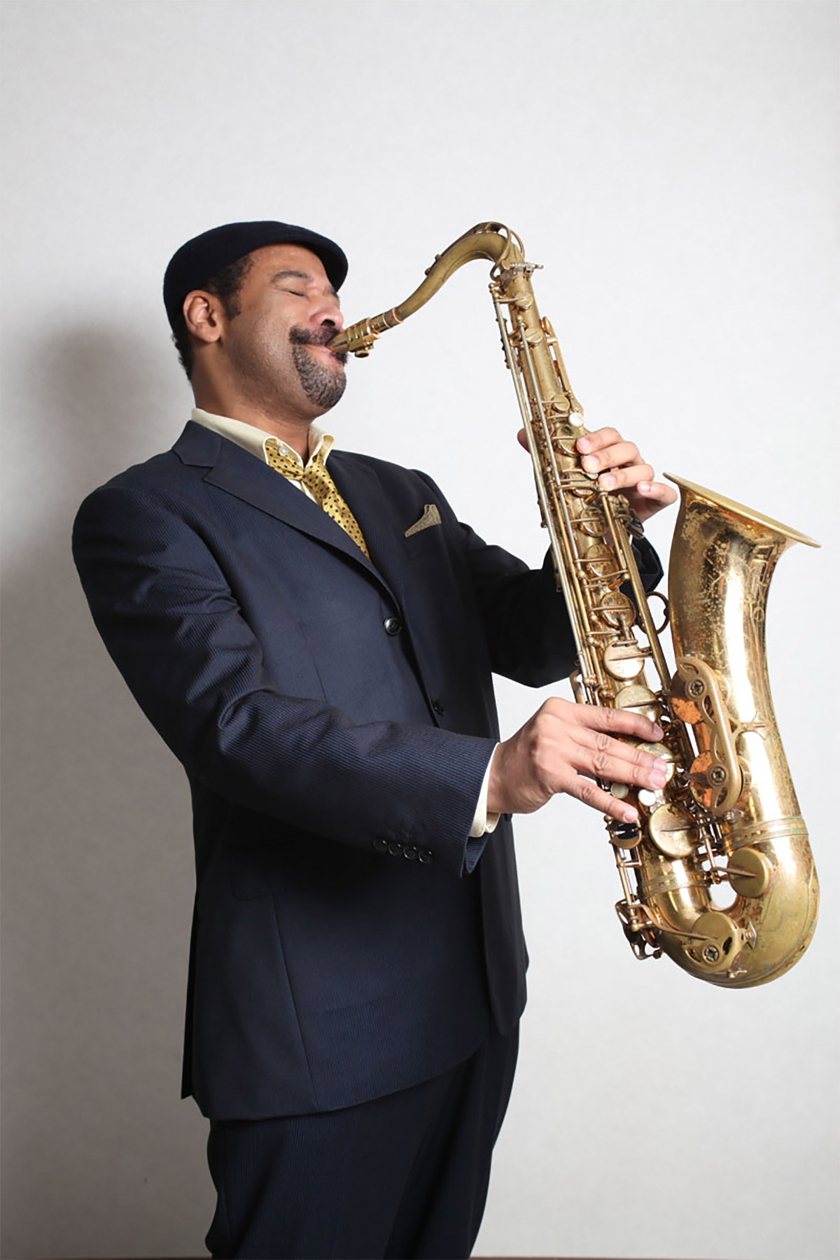 Tony Spruill playing tenor saxophone in a charcoal suit during a professional performance portrait.