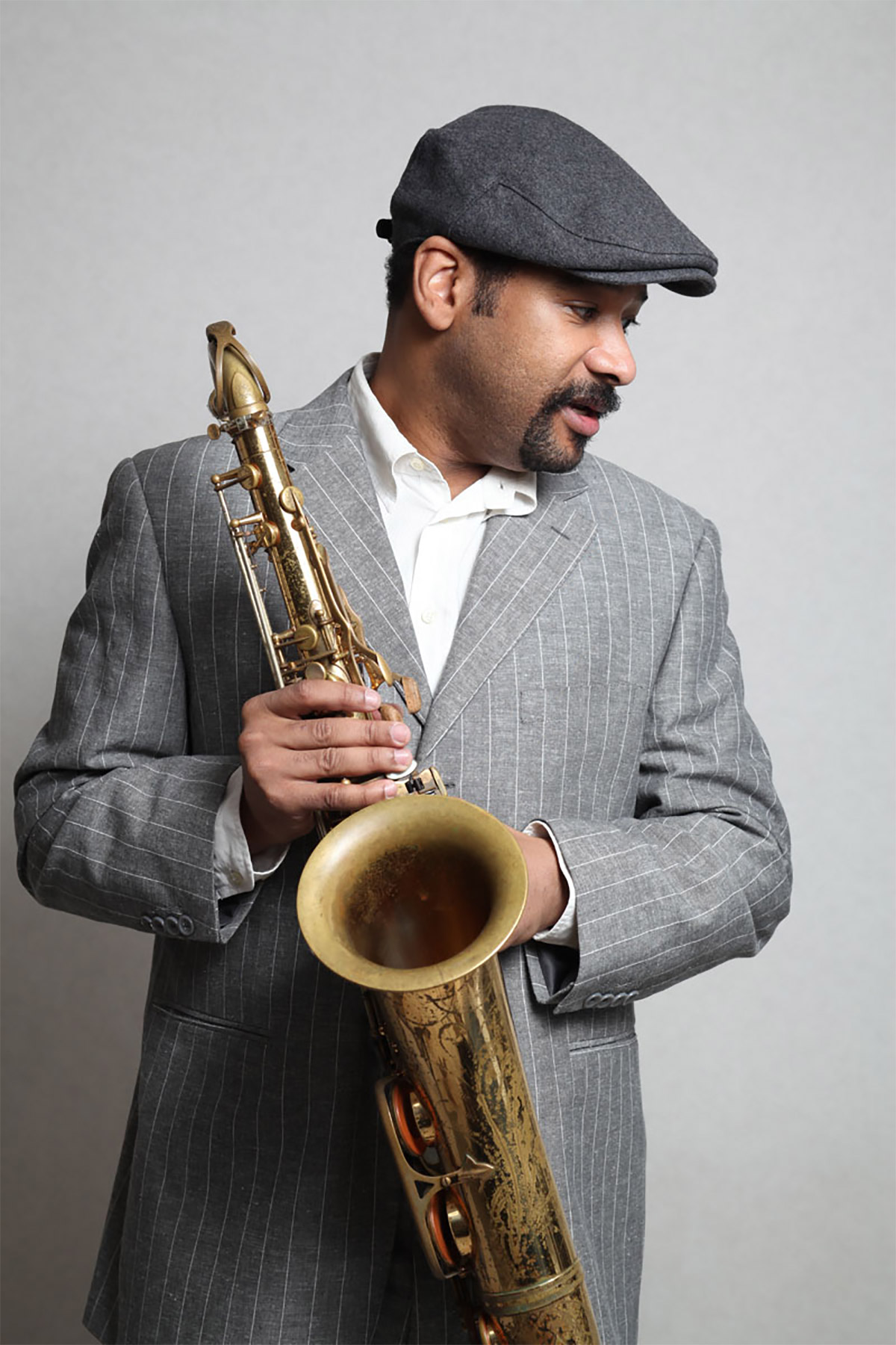 Tony Spruill holding a tenor saxophone in a grey suit for a professional musician portrait.